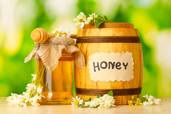 Солодкий мед в бочці і банку з квітами акації на дерев'яному столі на зеленому фоні — стокове фото