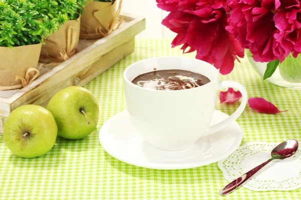 Xícara de chocolate quente, maçãs e flores na mesa no café — Fotografia de Stock
