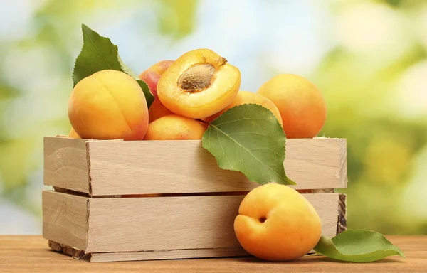 Mogna aprikoser med blad i trälåda på träbord på grön bakgrund — Stockfoto