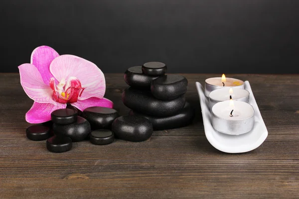 Spa kamienie z orchidea kwiat i świece na drewnianym stole na szarym tle — Zdjęcie stockowe