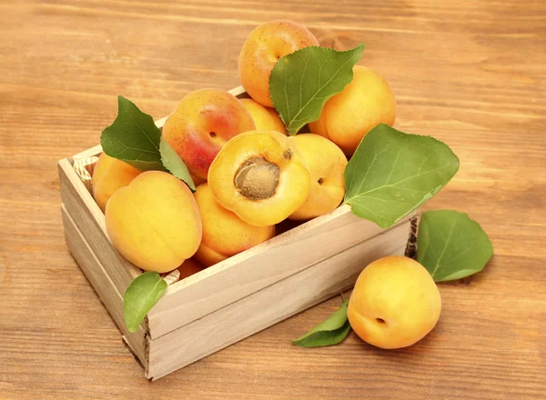 Rijp abrikozen met groene bladeren in houten doos op houten tafel — Stockfoto