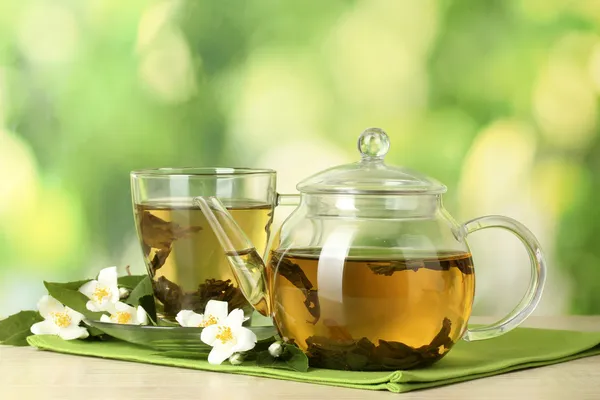 Tè verde con gelsomino in tazza e teiera su tavolo di legno su sfondo verde — Foto Stock