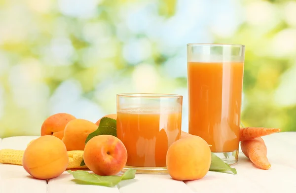 Gläser mit Karotten und Aprikosensaft auf weißem Holztisch auf grünem Hintergrund — Stockfoto