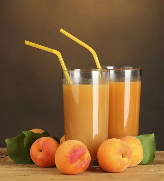 Glasses of apricot juice on wooden table on brown background — Stock Photo, Image