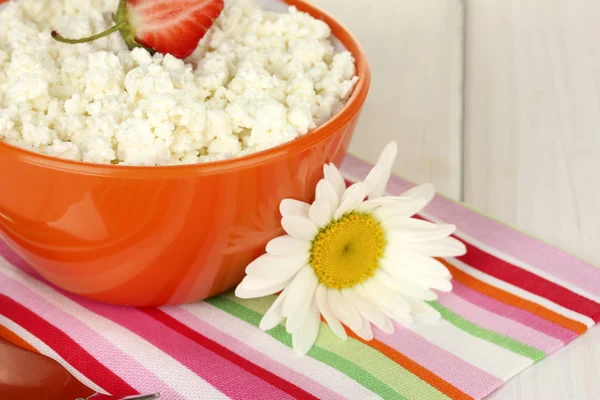 Cottage cheese with strawberry in orange bowl, fork and flower on colorful napkin on white wooden table close-up — Stock Photo, Image