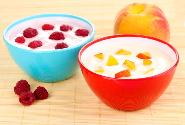 Yogurt dengan buah persik dan raspberry dalam mangkuk di tikar bambu — Stok Foto