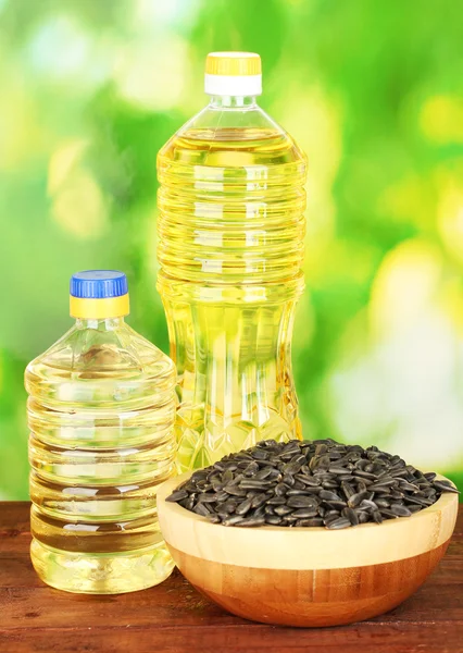 Подсолнечное масло в бутылках с семенами подсолнечника на зеленом фоне крупным планом — стоковое фото