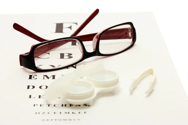 Brýle, kontaktní čočky v nádobách a pinzety na pozadí snellen oko grafu — Stock fotografie