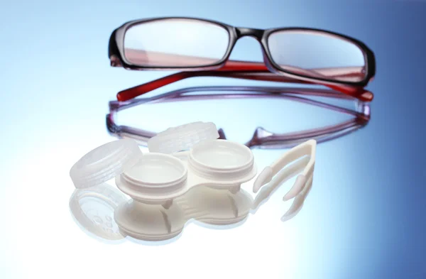 Okulary, soczewki kontaktowe, w pojemnikach i pincety na niebieskim tle — Zdjęcie stockowe