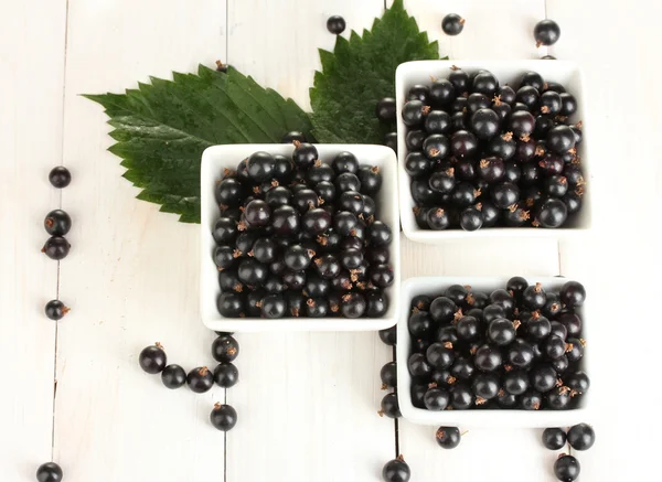 Färska svarta vinbär i trä skålar på vit trä bakgrund närbild — Stockfoto