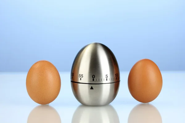 Temporizador de ovos e ovos no fundo azul — Fotografia de Stock
