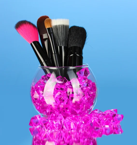 Make-up borstels in een kom met stenen op blauwe achtergrond — Stockfoto