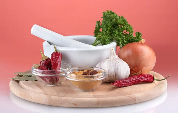 Sammansättningen av vit mortel och stöt med kryddor och grönsaker på skärbräda på röd bakgrund — Stockfoto