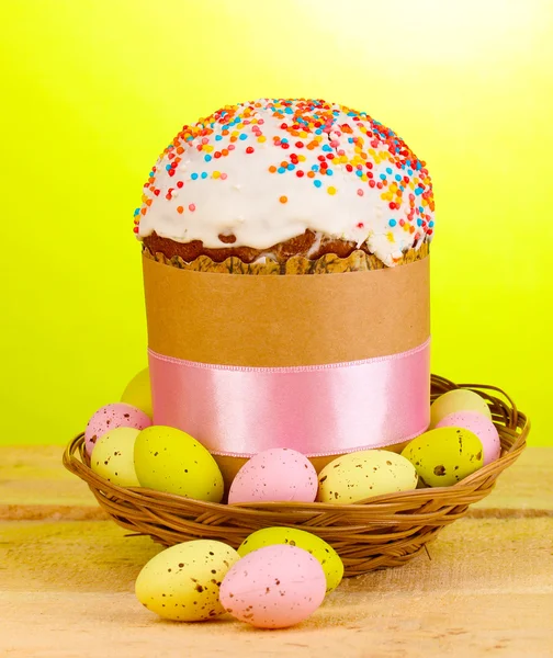 Beautiful Easter cake in basket with eggs on wooden table on green background — Stock Photo, Image