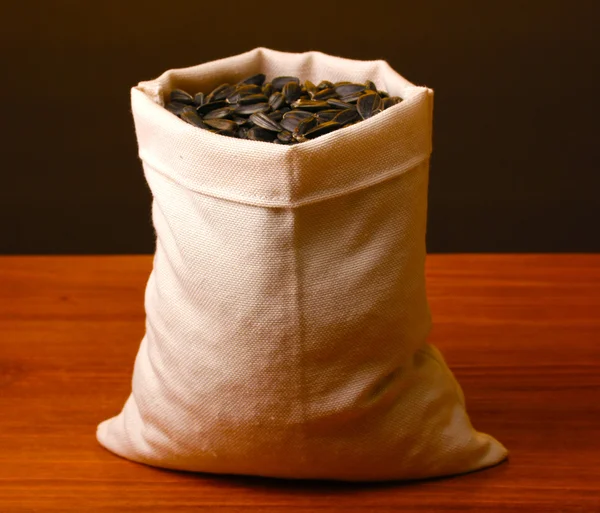 Cloth bag of sunflower seeds on wooden table on brown background