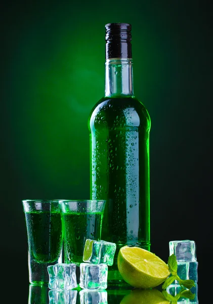 Флакон и стаканы абсента с лаймом и льдом на зеленом фоне — стоковое фото
