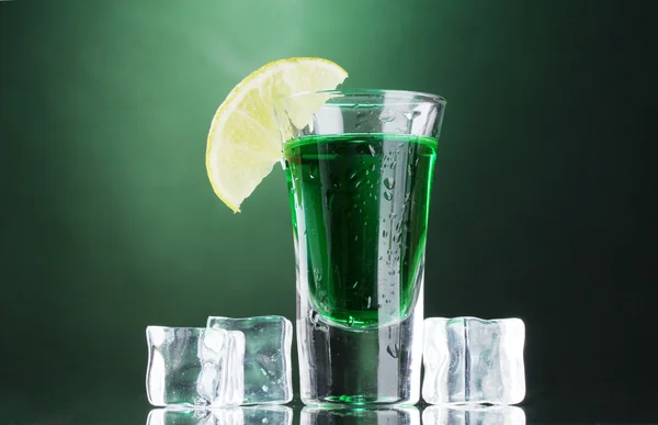 Стакан абсента, лайма и льда на зеленом фоне — стоковое фото