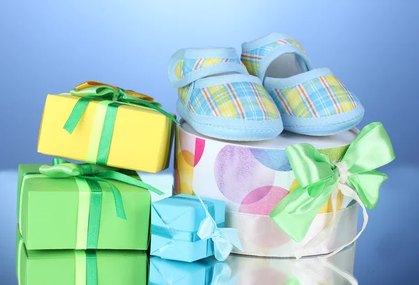 Beautiful gifts and baby's bootees on blue background — Stock Photo, Image