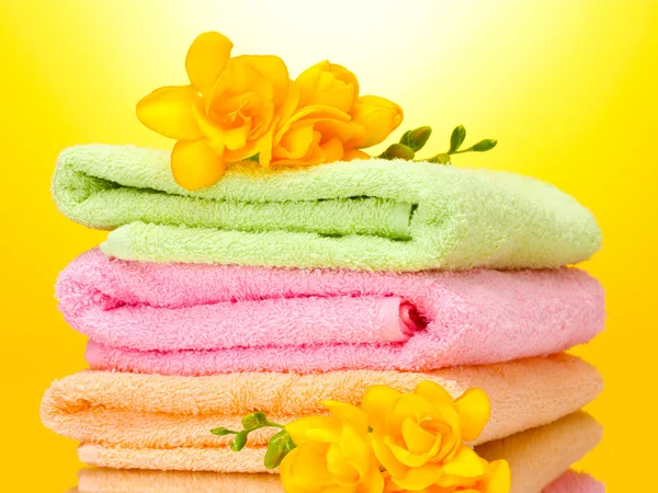 पिवळा पार्श्वभूमीवर रंगीत टॉवेल्स आणि फुले — स्टॉक फोटो, इमेज