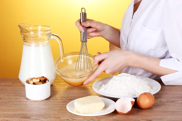 stock image Female hands mixing eggs in bowl on wooden table on yellow background