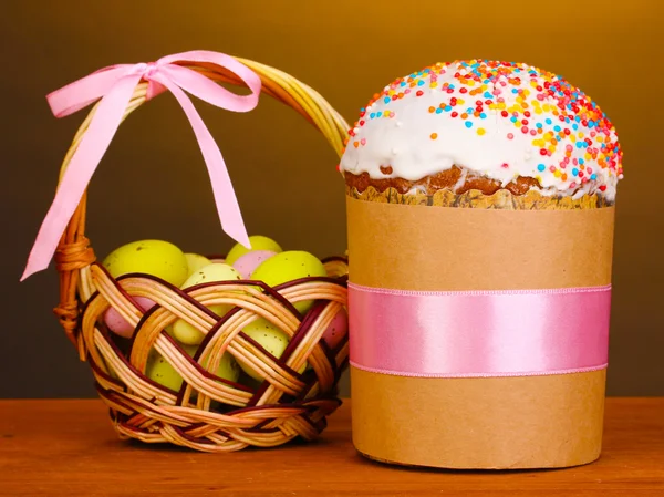 Beautiful Easter cake with eggs in basket on wooden table on brown background — Stock Photo, Image