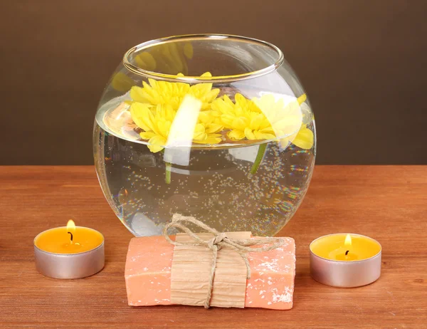 Composition Spa de bougies lumineuses et morceau de savon et chrysanthème jaune flottant sur fond en bois — Photo