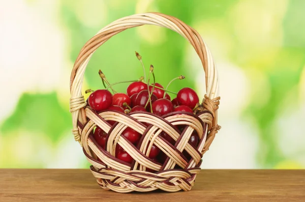 Körsbär i korg på träbord på grön bakgrund — Stockfoto