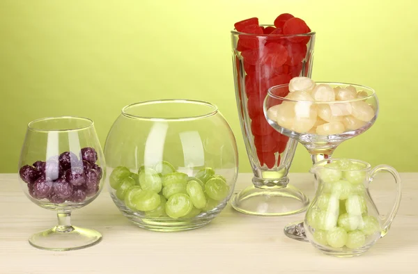 Caramelle a colori in bicchieri su tavolo di legno su sfondo verde — Foto Stock