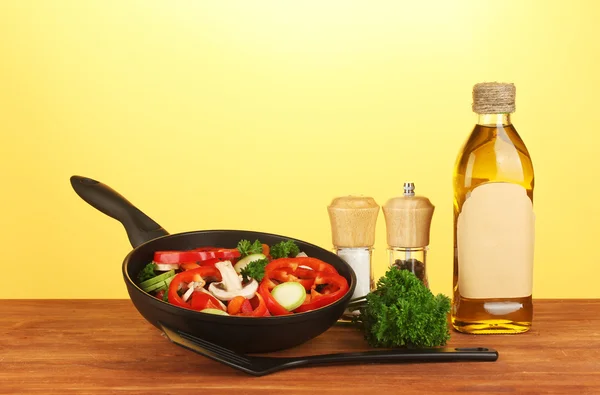 Frying pan with vegetables on yellow background — Stock Photo, Image