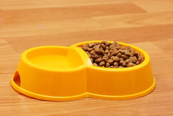 Torr kattmat och vatten i gul skål på golvet — Stockfoto