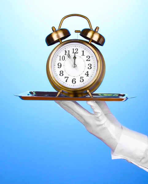 Hand in de handschoen houden zilveren dienblad met wekker op blauwe achtergrond — Stockfoto