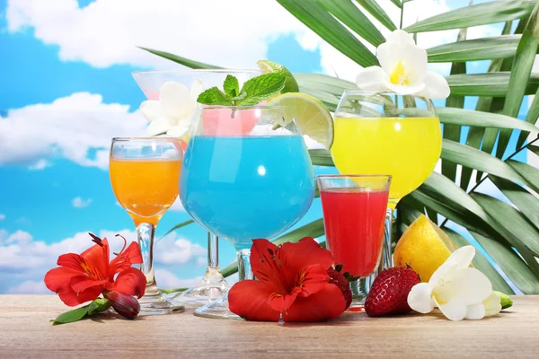 Cocktail esotici e fiori sul tavolo su sfondo cielo blu — Foto Stock