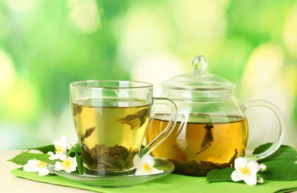 Зеленый чай с жасмином в чашке и чайник на деревянном столе на зеленом фоне — стоковое фото