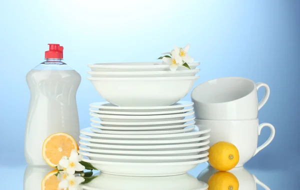 Pusty czyste talerze i kubki z naczyń płyn i cytryny na niebieskim tle — Zdjęcie stockowe
