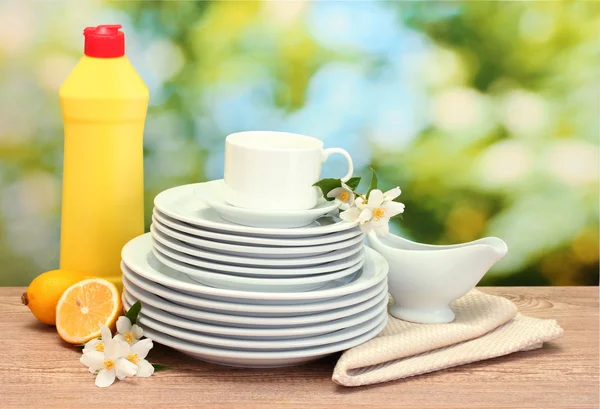 Pratos limpos vazios e copos com líquido de lavar louça, flores e limão na mesa de madeira em fundo verde — Fotografia de Stock