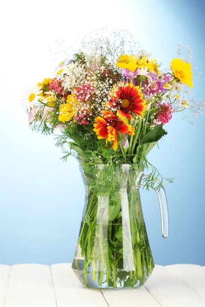 Hermoso ramo de flores silvestres brillantes en jarrón de vidrio, sobre mesa de madera sobre fondo azul — Foto de Stock