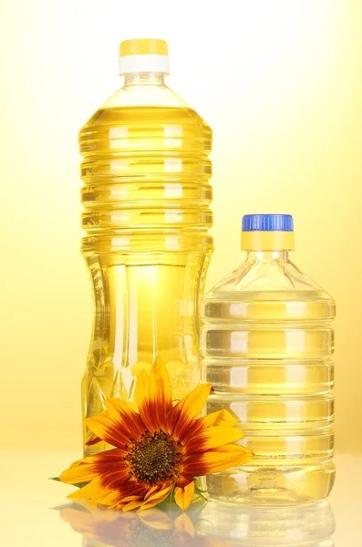 Sonnenblumenöl und Sonnenblumen auf gelbem Hintergrund — Stockfoto