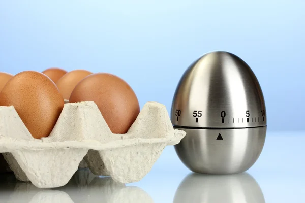 Eieren in doos en ei timer op blauwe achtergrond — Stockfoto