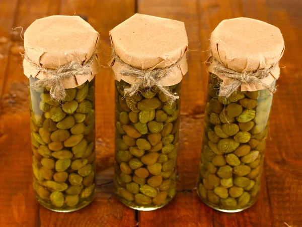 Frascos de vidrio con alcaparras en conserva sobre fondo de madera de cerca —  Fotos de Stock