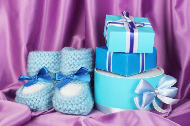 Blue baby boots and gifts on silk background clipart