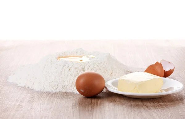 Oeuf dans la farine sur table en bois et beurre sur assiette sur fond blanc — Photo