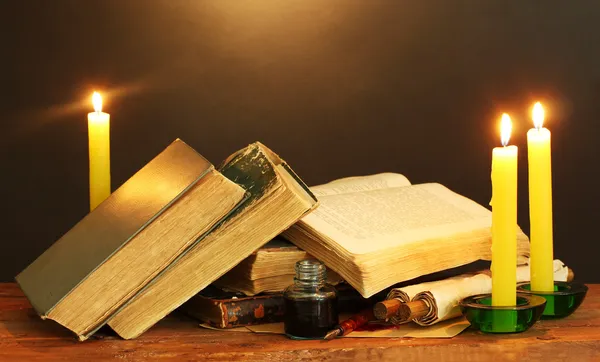 Vecchi libri, pergamene, calamaio penna inchiostro e candele su tavolo di legno su sfondo marrone — Foto Stock