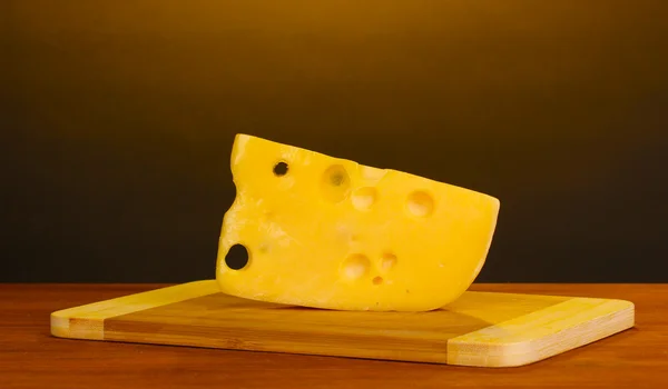 茶色の背景に木製のテーブルでまな板の上のチーズ — ストック写真
