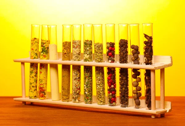A fából készült asztal a sárga háttér csövek különböző fűszerek — Stock Fotó