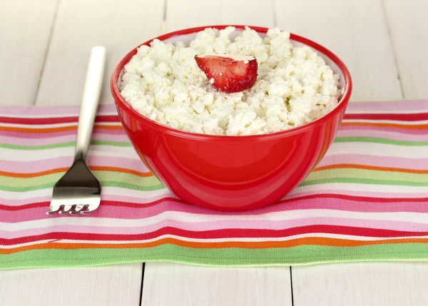 Cottage cheese with strawberry in red bowl and fork on colorful napkin on white wooden table close-up — Stock Photo, Image