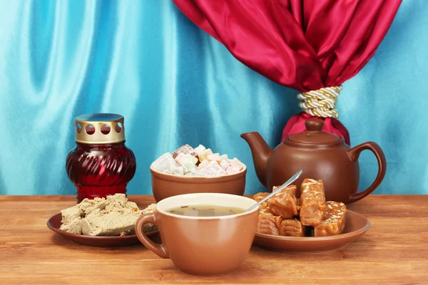 Tetera con taza y platillos con dulces orientales - sorbete, halva y deleite turco en la mesa de madera sobre un fondo de cortina primer plano —  Fotos de Stock