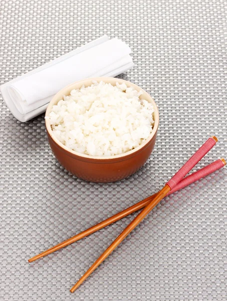 Kom rijst en eetstokjes op grijs mat — Stockfoto