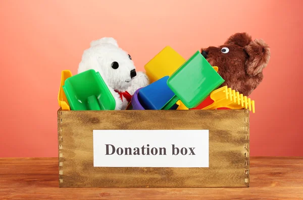 Donatie box met kinderen speelgoed op rode achtergrond close-up — Stockfoto