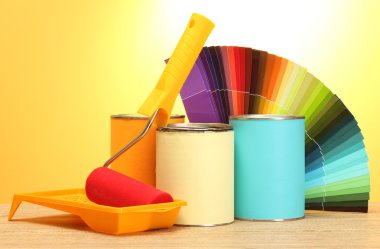 Tin cans with paint, roller, brushes and bright palette of colors on wooden table on yellow background clipart