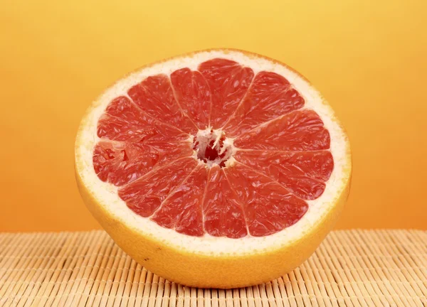 De helft van rijp grapefruit op bamboe mat op gele achtergrond — Stockfoto